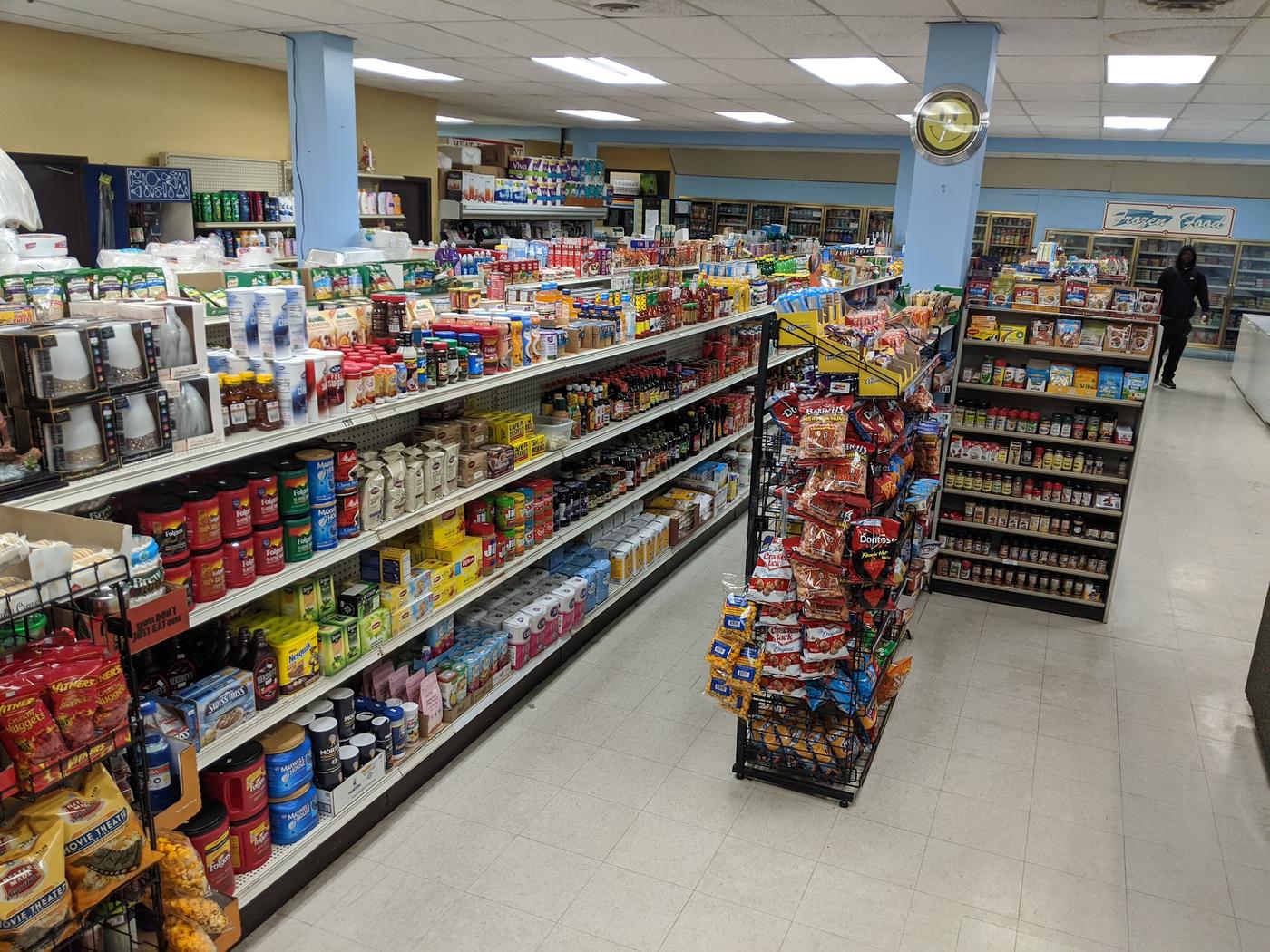 An aisle inside N&M Food Market, shelves stocked with groceries running back towards the coolers and a frozen food sign